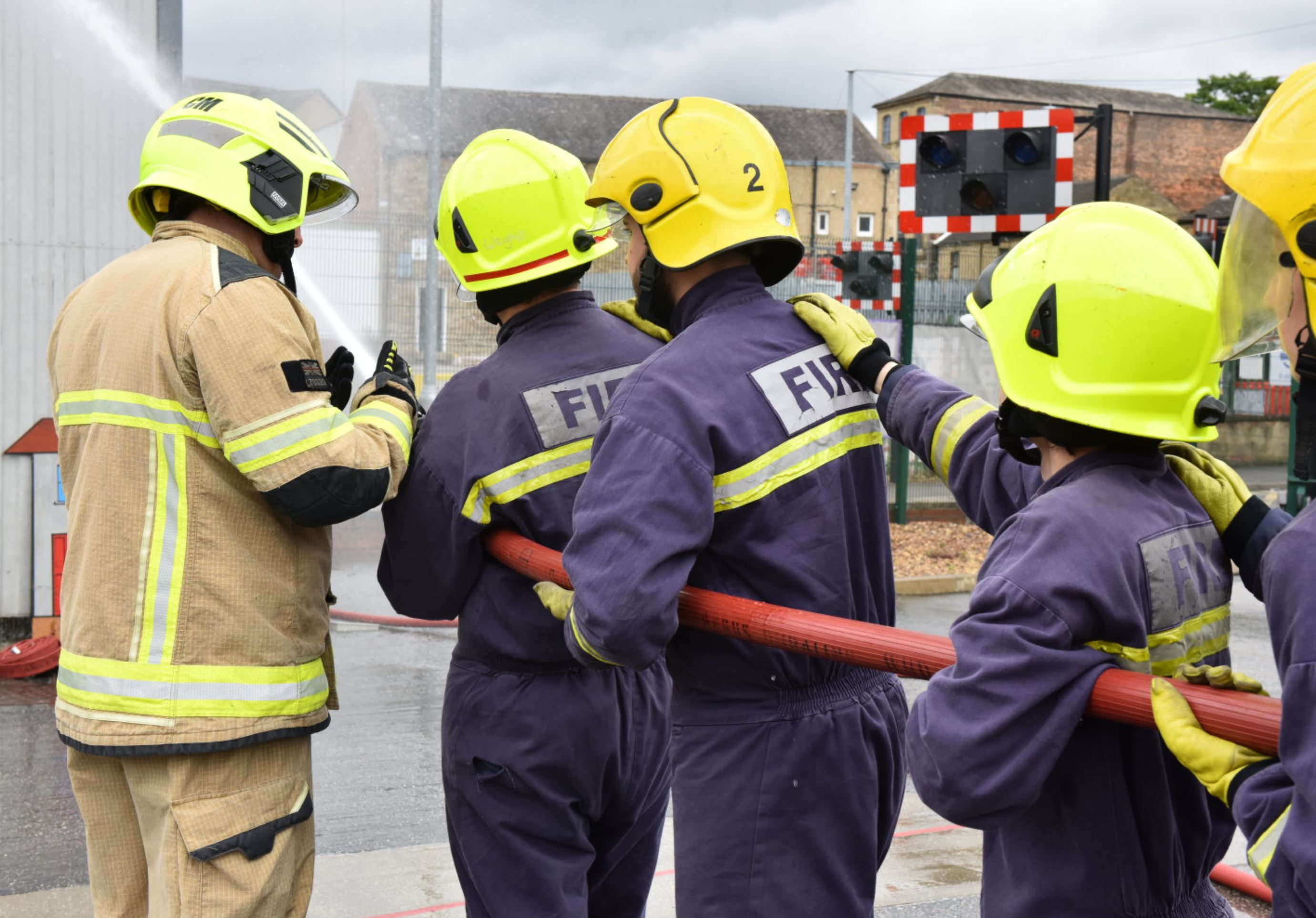 3 young adults holding fire hose with support of firefighter in full kit